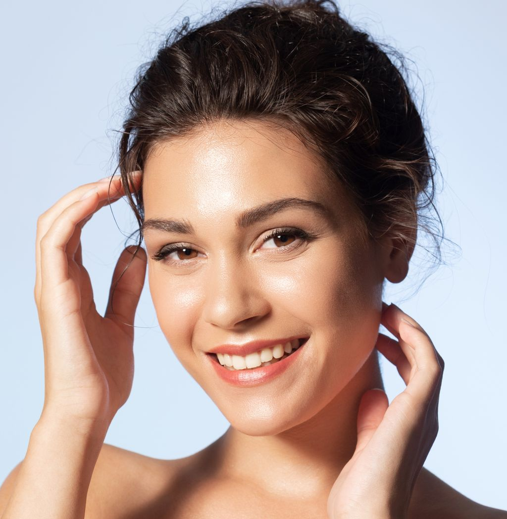 Woman smiling, hands near face, against a soft blue background.