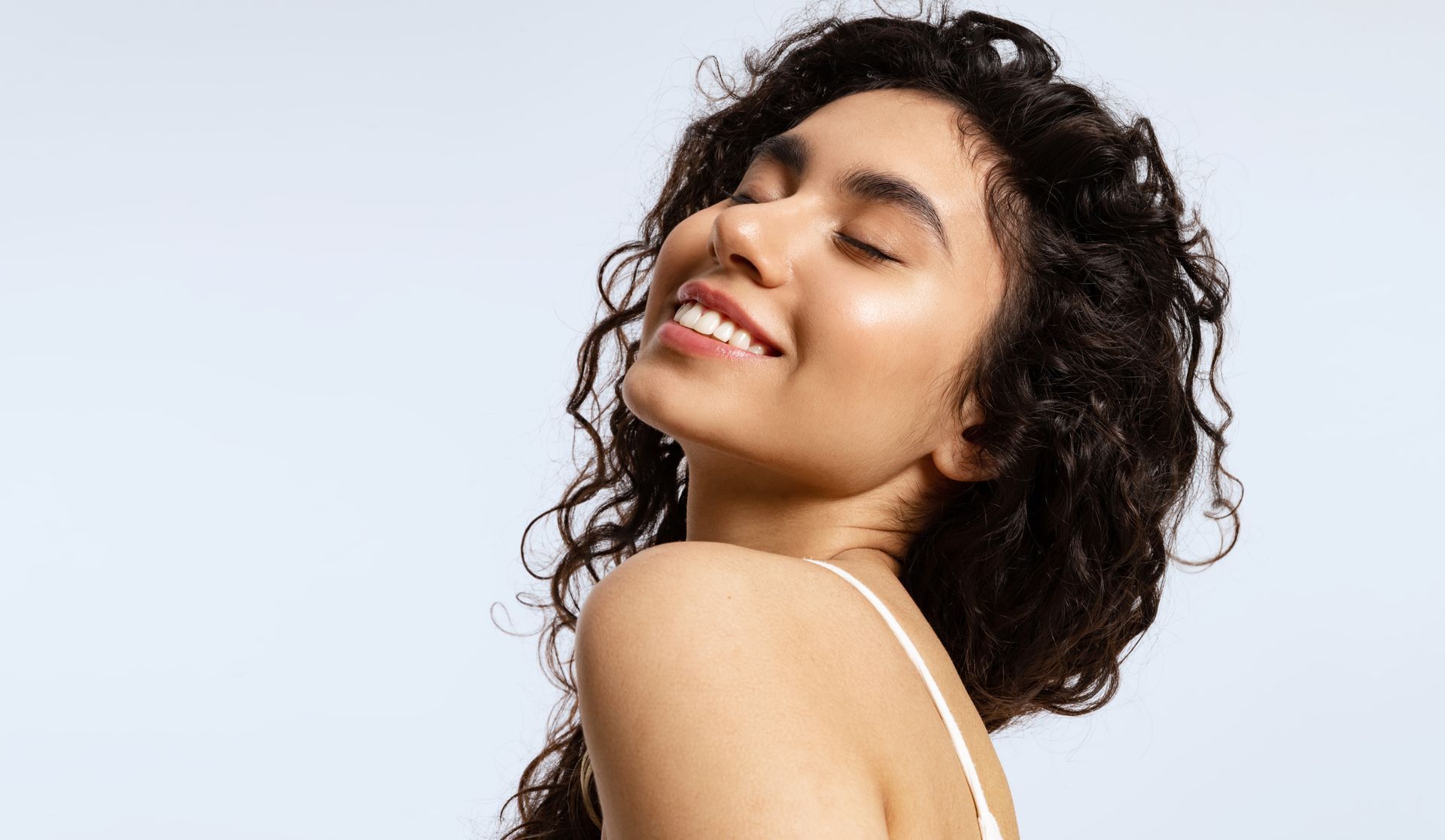 A woman with curly hair is smiling with her eyes closed.