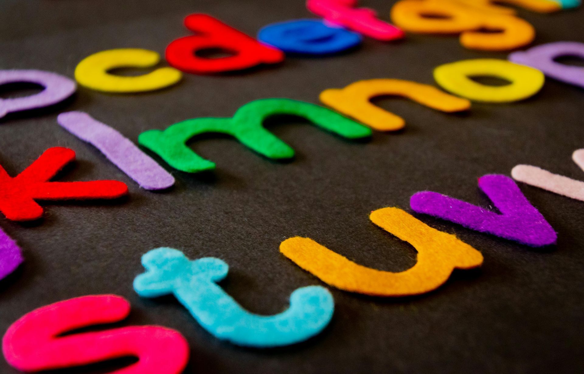 Colorful felt alphabet letters scattered on a black surface.