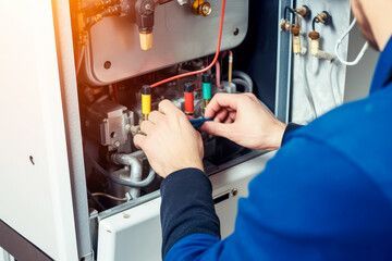 A man is working on a boiler with a screwdriver.