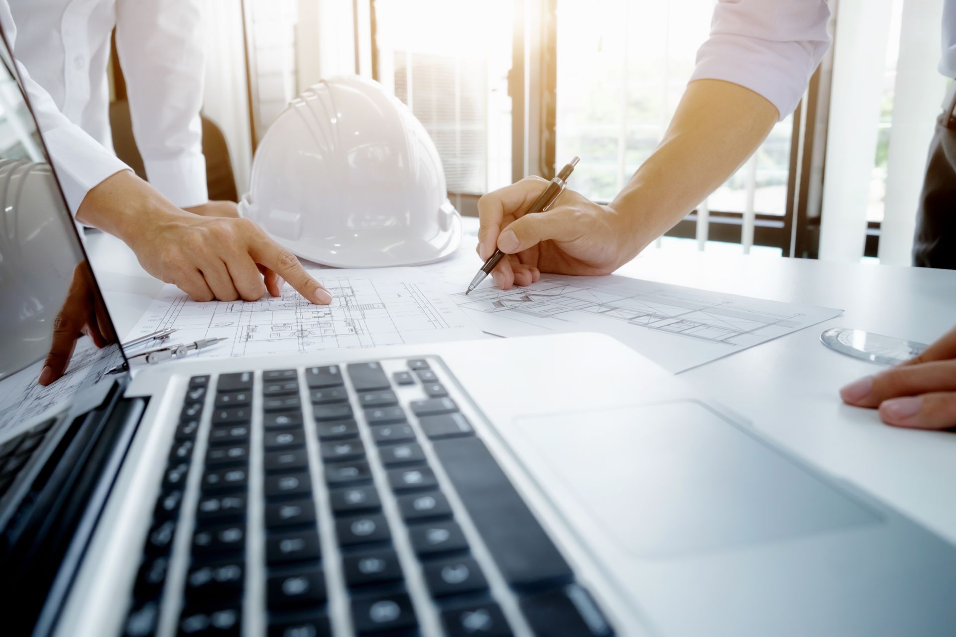 Two construction workers in hard hats reviewing plans at a job site near heavy machinery.