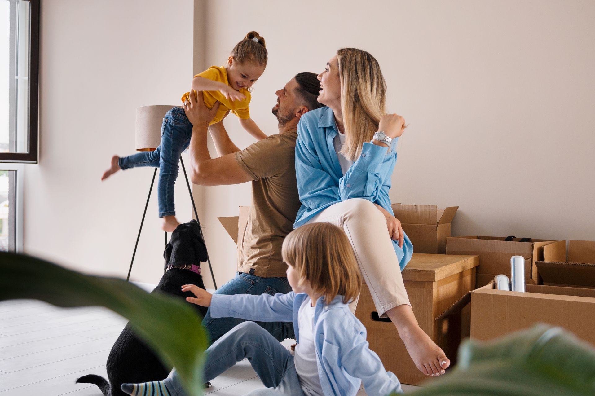 Family playing together on a couch in a bright living room, with a child lifted in the air