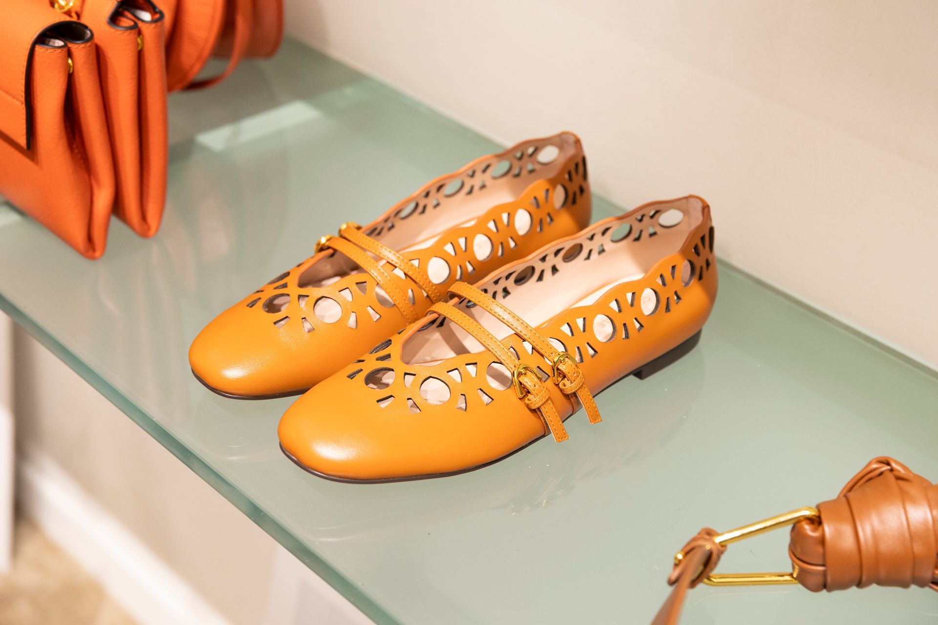 Ballerine arancioni sagomate esposte su una mensola di vetro, con accessori coordinati nelle vicinanze.