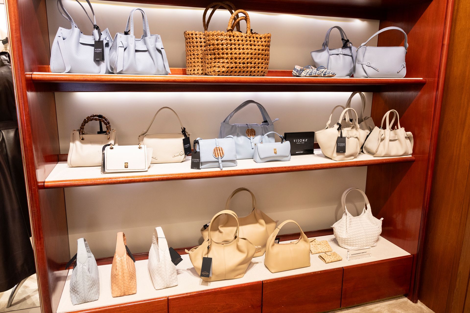 Borse esposte su scaffali di legno in una boutique, perlopiù bianche e beige, con una borsa in vimini.