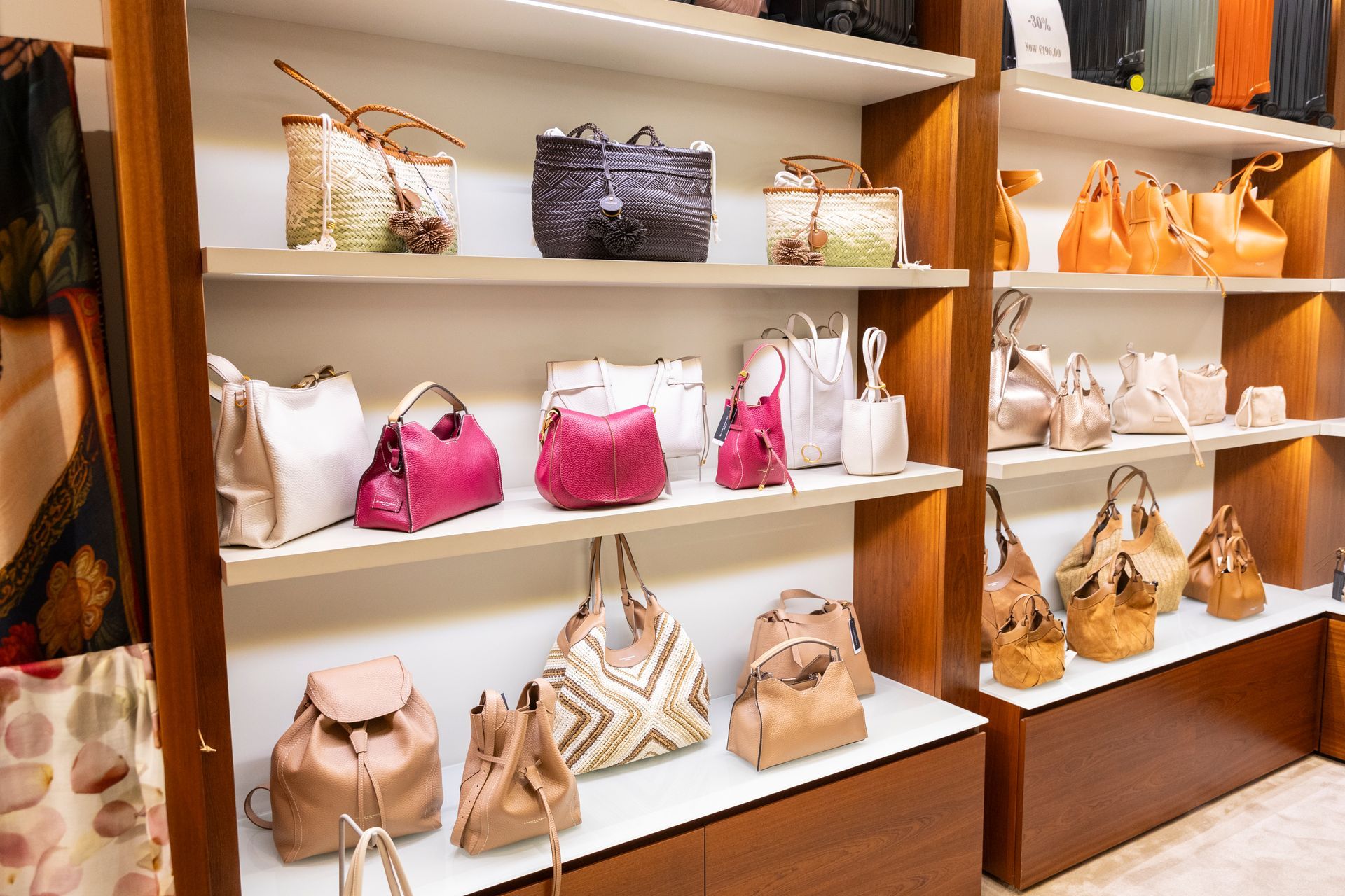 Borse esposte sugli scaffali di una boutique nei toni del bianco, del beige, del rosa e dell'arancione.