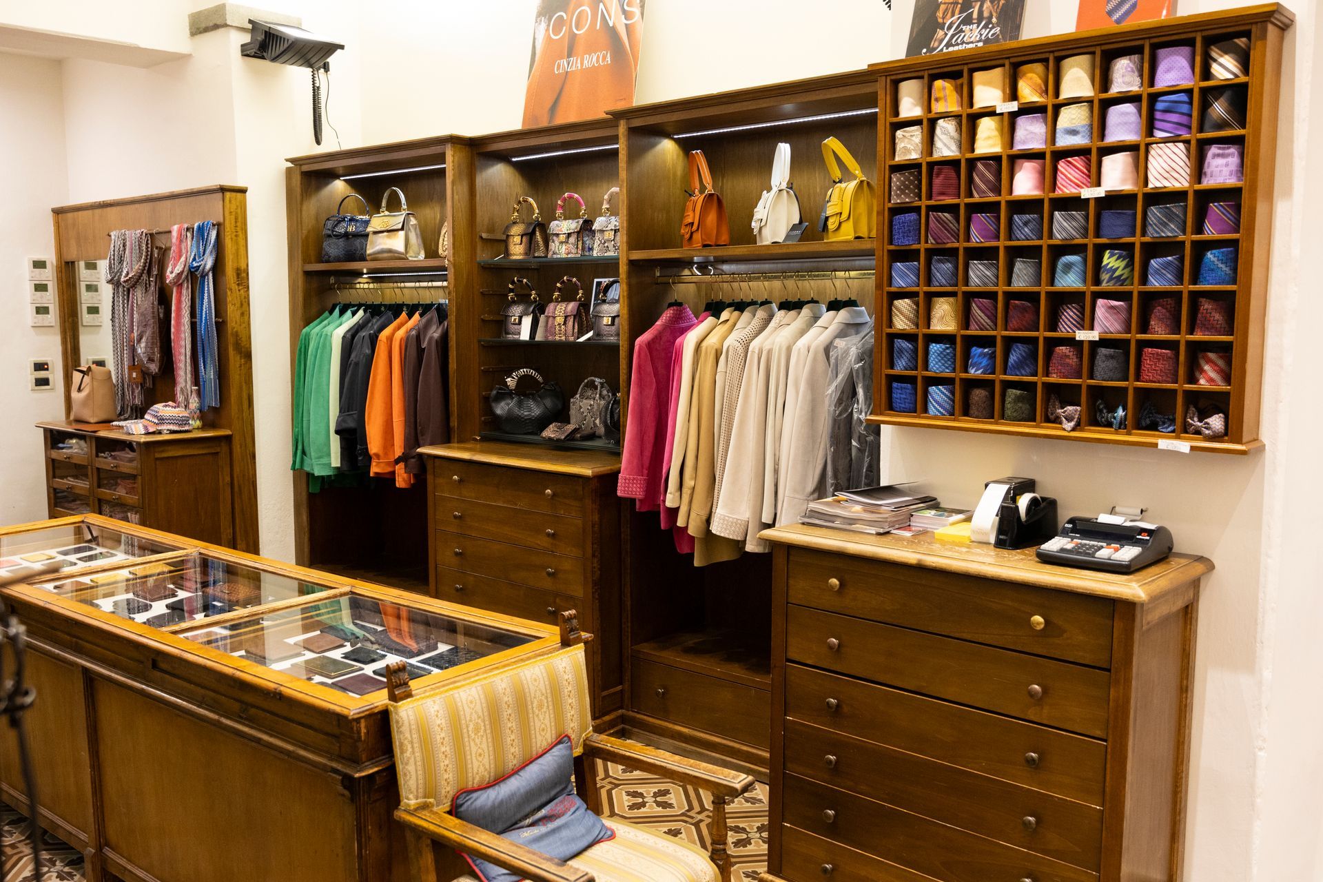 Interno di una boutique con appendiabiti, cassetti in legno, scaffali con accessori colorati e una vetrina.