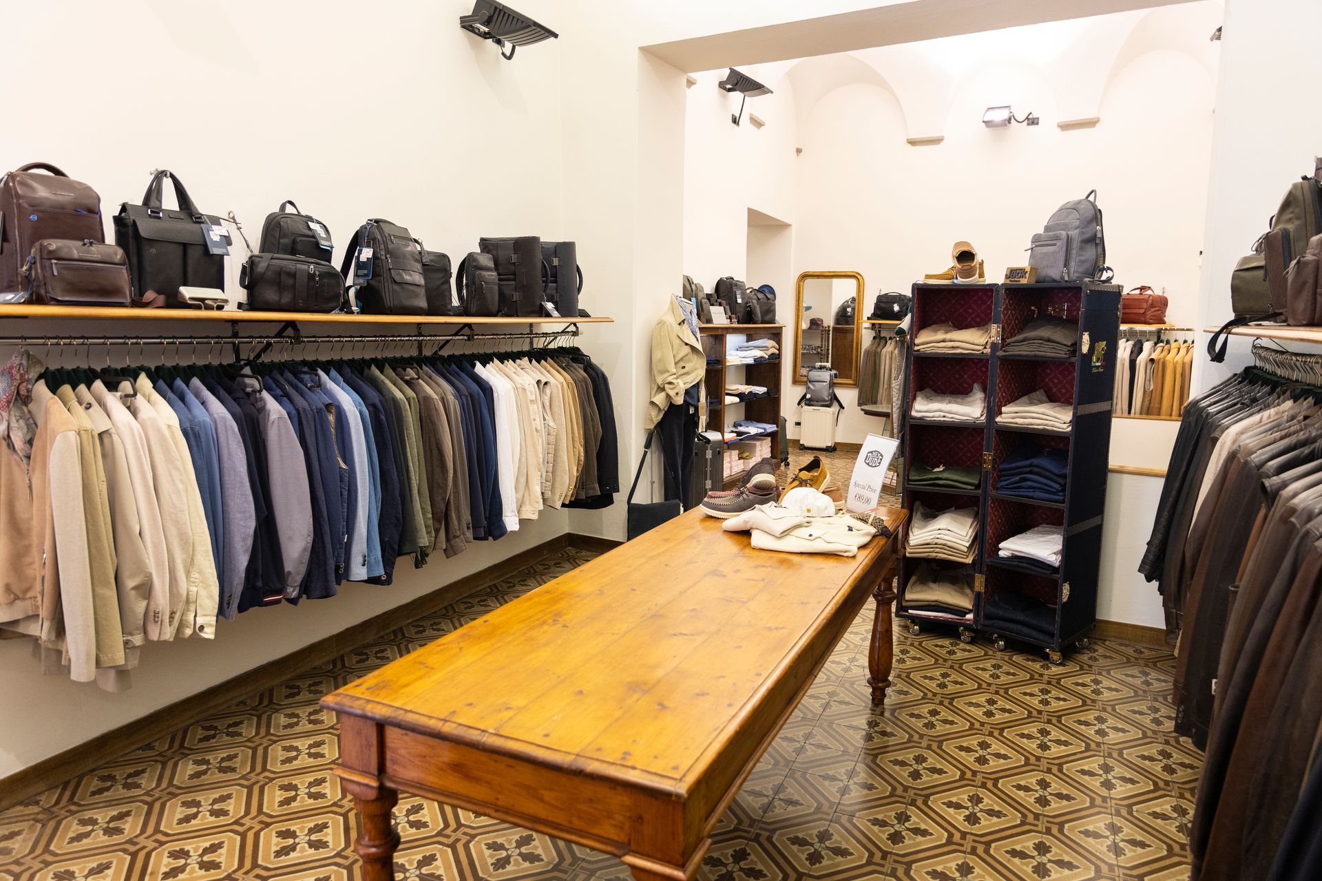 Interno di una piccola boutique con appendiabiti, scaffali per borse e un tavolo di legno al centro.