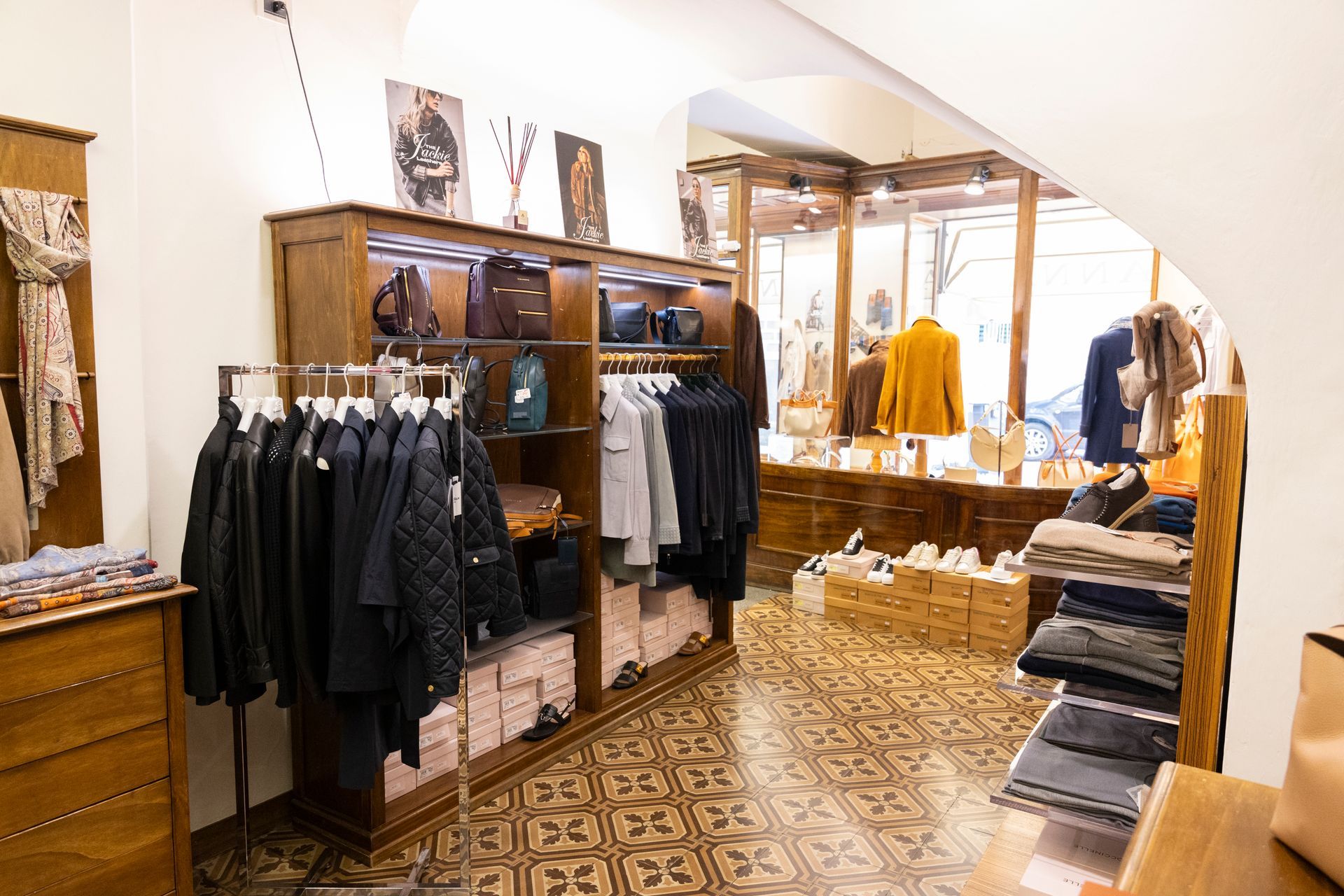 Negozio di abbigliamento boutique con scaffali pieni di giacche scure, maglioni piegati e vetrine a specchio.