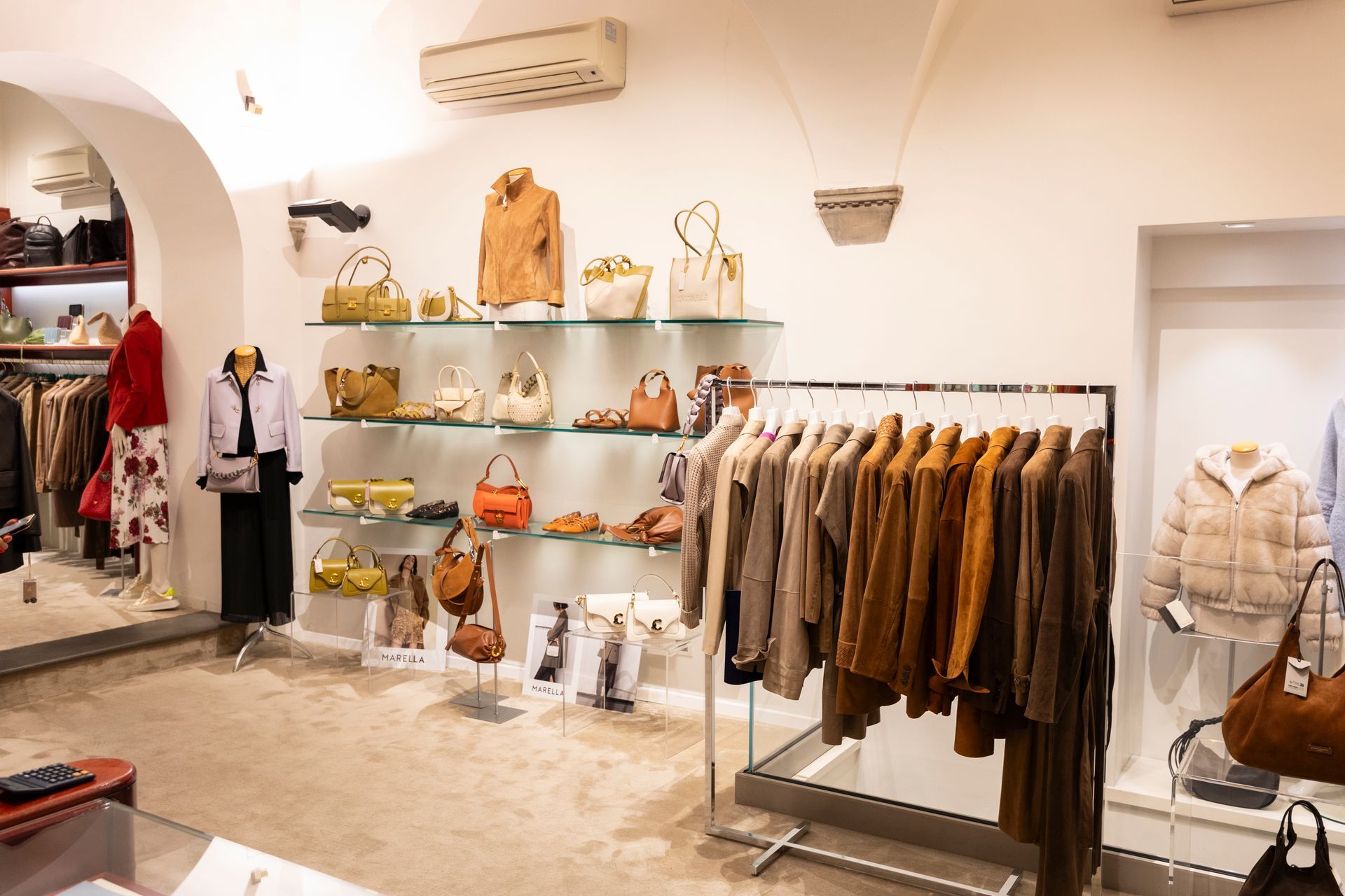 Negozio di abbigliamento boutique con cappotti dai toni neutri esposti su appendiabiti e scaffali in un interno luminoso e minimalista.