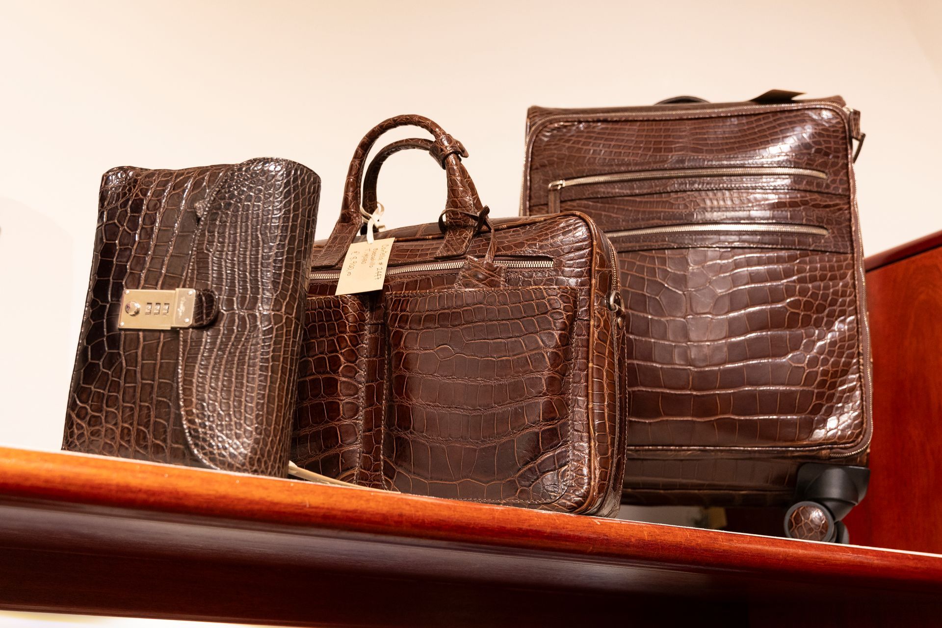 Tre borse in pelle marrone, con texture effetto coccodrillo e chiusure dorate, esposte su uno scaffale.