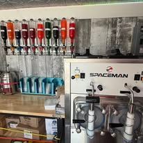 Coffee shop drink station with red and blue syrup pumps, cups, and a Spaceman machine on the counter