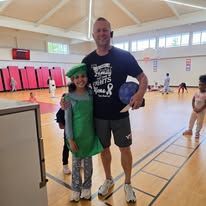 Adult and child posing in a gym, child in green costume and adult holding a basketball