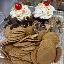 Ice cream sundae with whipped cream, cherries, chocolate, and stacked waffle cookies on a tray