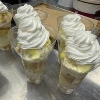 Three glasses of layered dessert topped with swirls of whipped cream on a tray