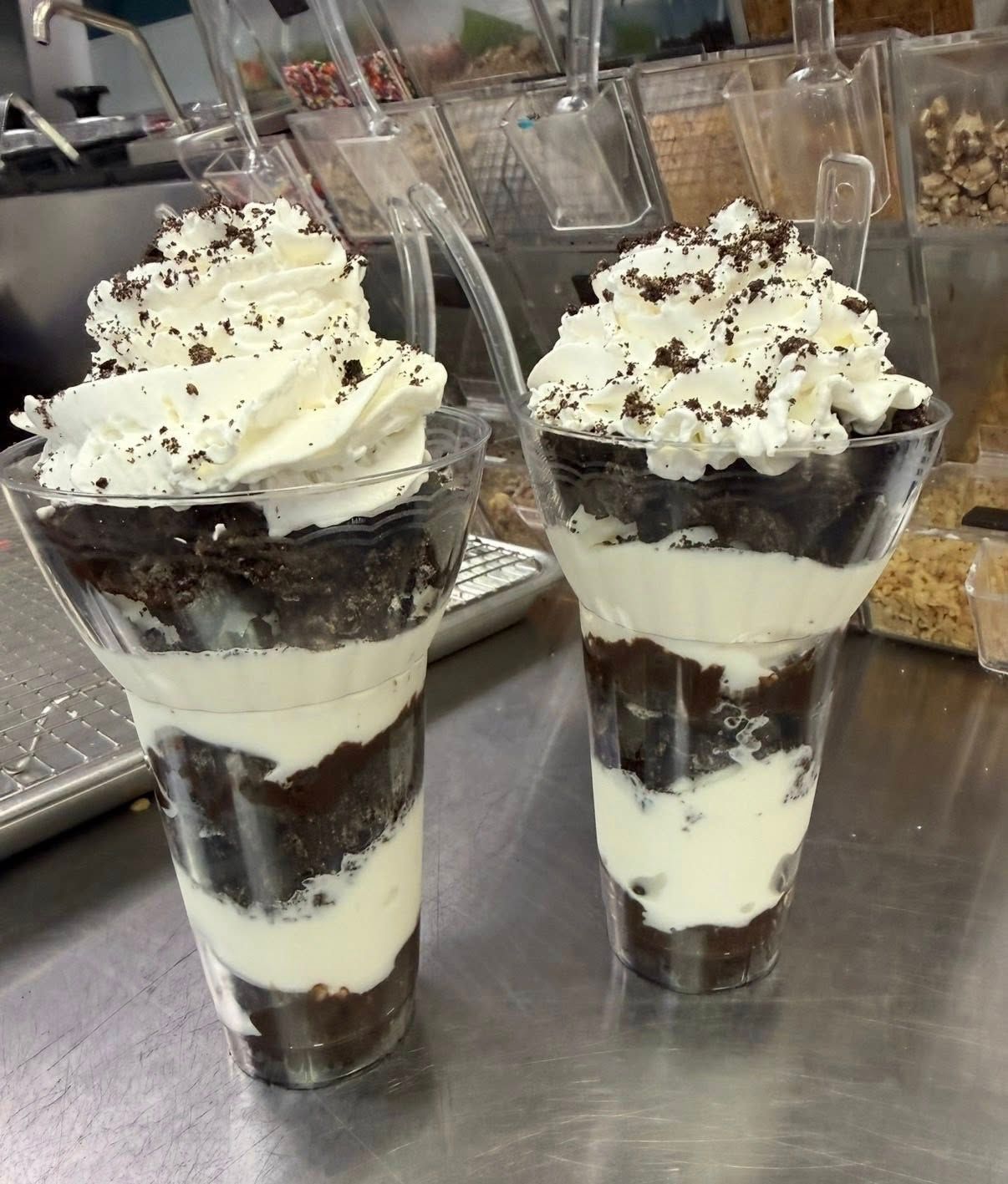Two chocolate parfaits in clear cups, layered with whipped cream and chocolate sprinkles on top.