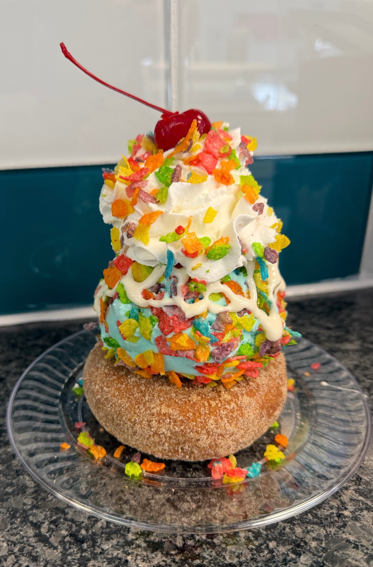 Ice cream sundae topped with whipped cream, fruit, and colorful sprinkles on a glass plate