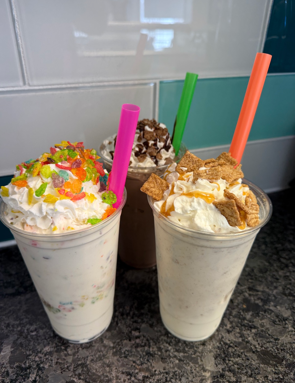Three colorful milkshakes topped with whipped cream and sprinkles on a countertop.