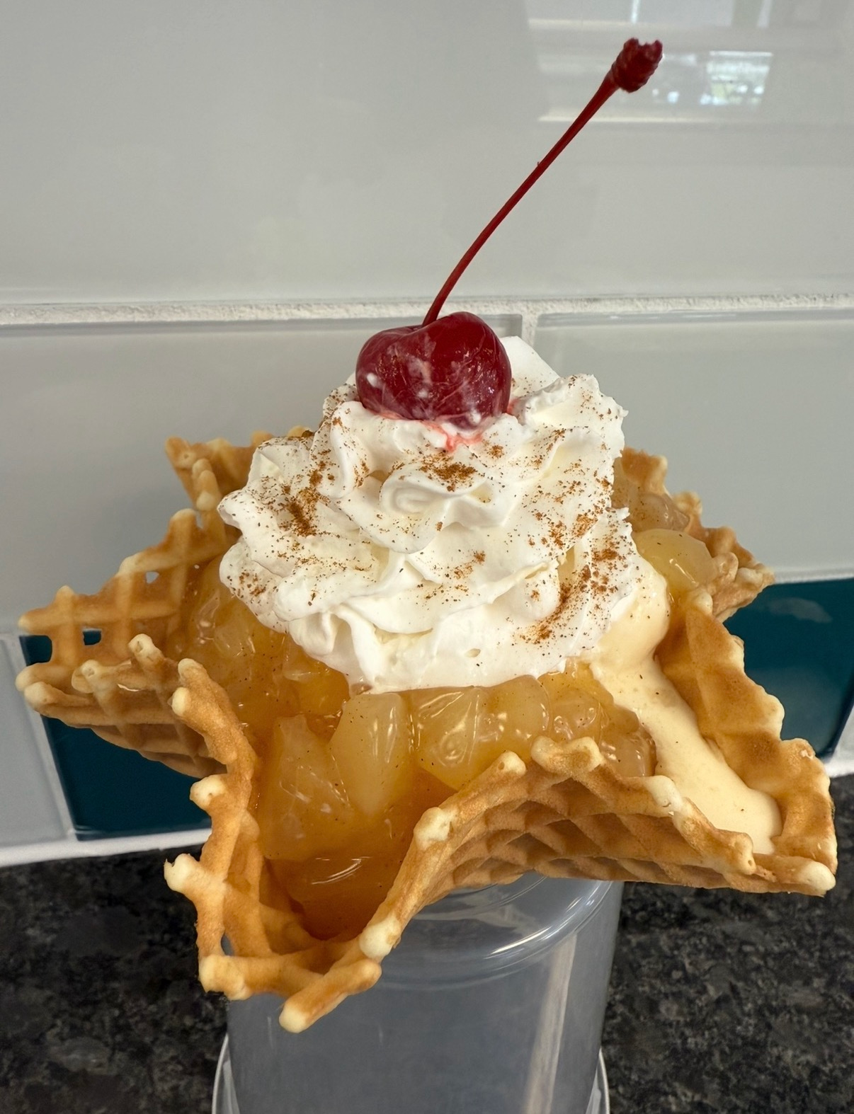 Waffle bowl topped with whipped cream, cherry, and caramel sauce on a countertop