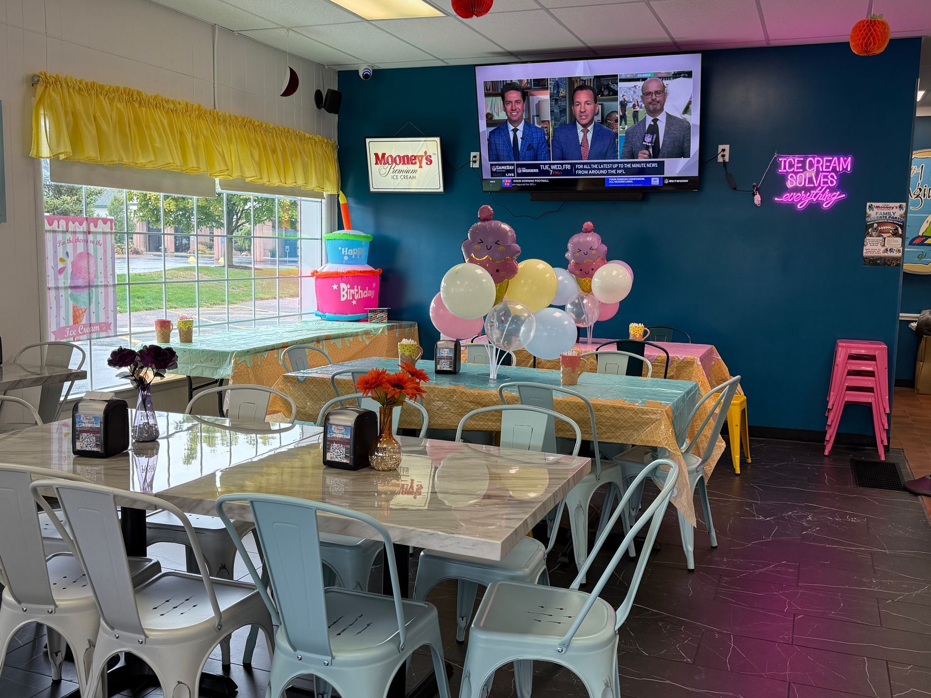 Decorated birthday party table with cake, balloons, bunting, and guests in a cozy cafe