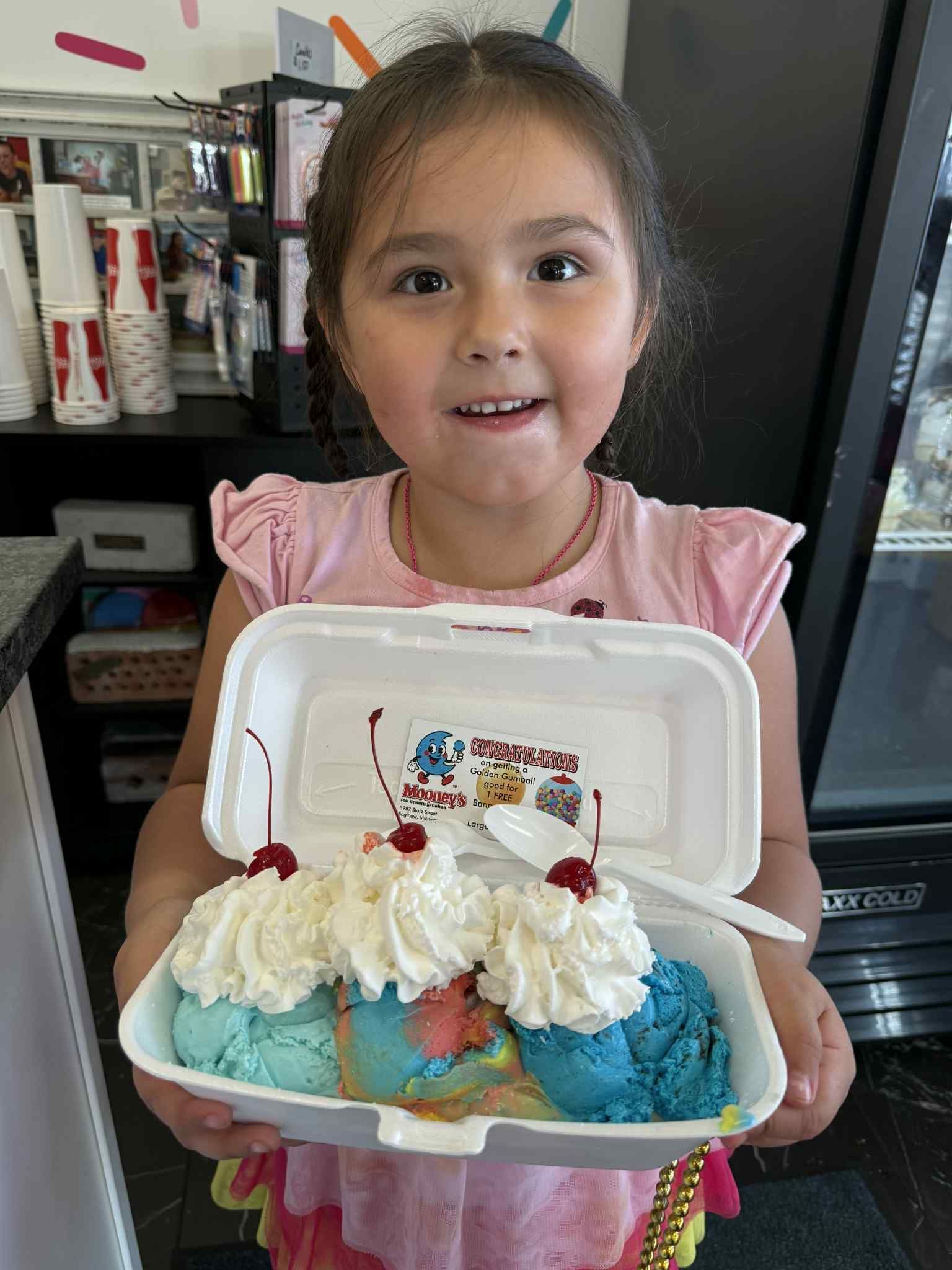 Child holding a decorated cupcake cake in a white box, smiling indoors.