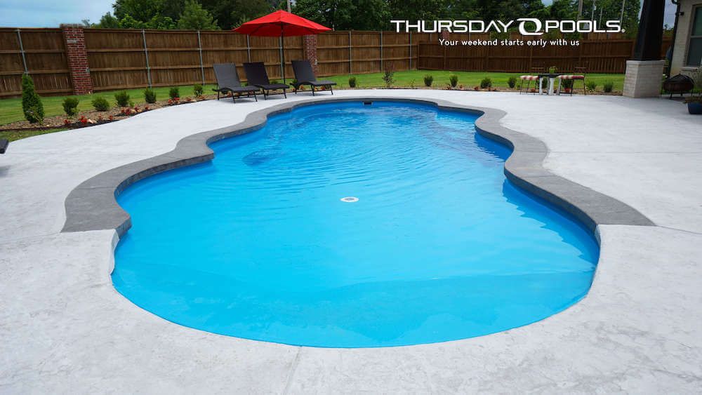 Outdoor swimming pool with bright blue water, gray deck, and red umbrella in a fenced backyard