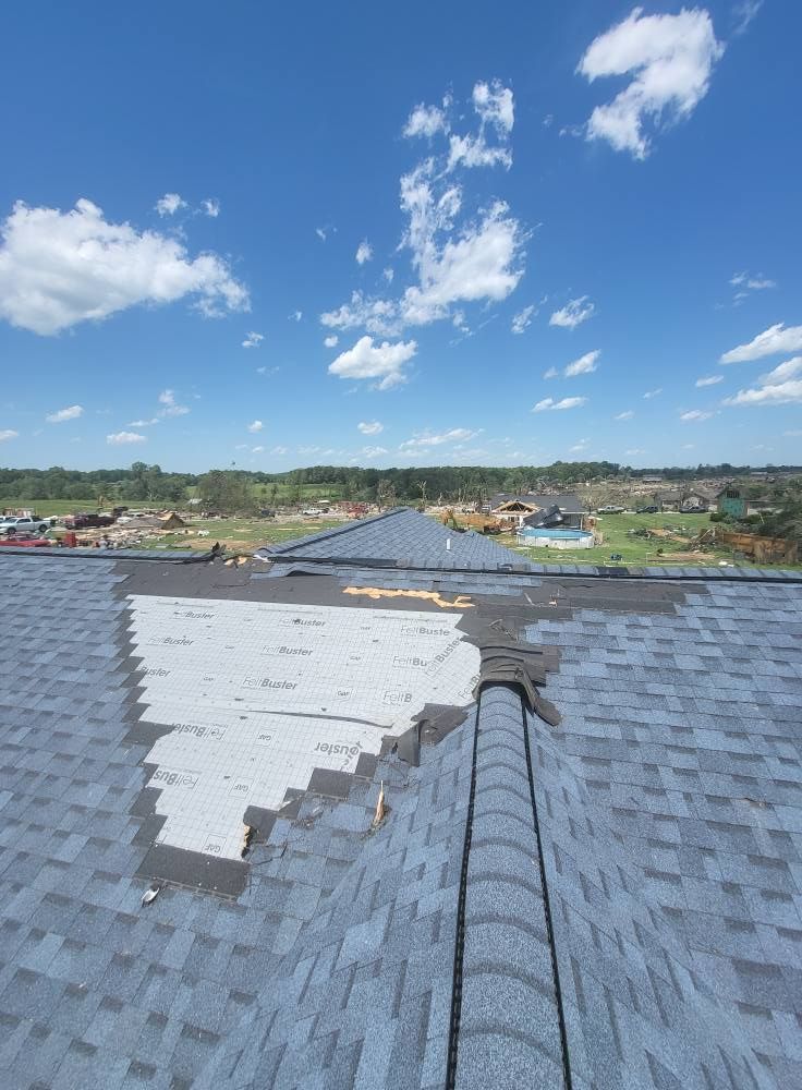 Roof with missing shingles under a blue sky, revealing the underlayment.
