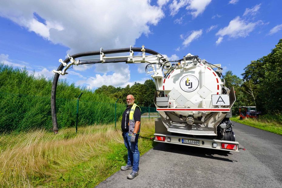 Ein Mann steht neben einem Saugwagen am Straßenrand.