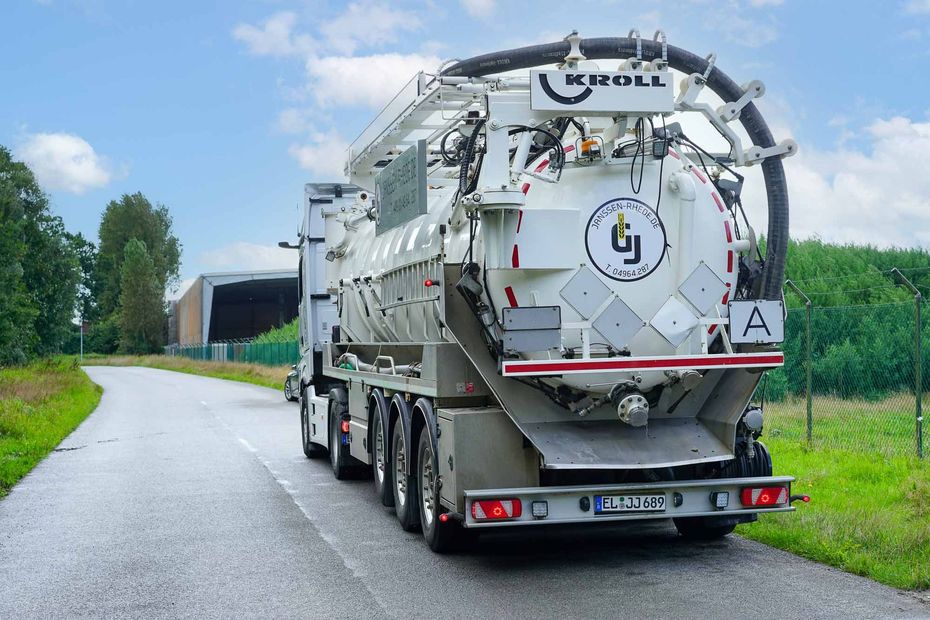 Ein großer Saugwagen fährt eine Straße entlang.