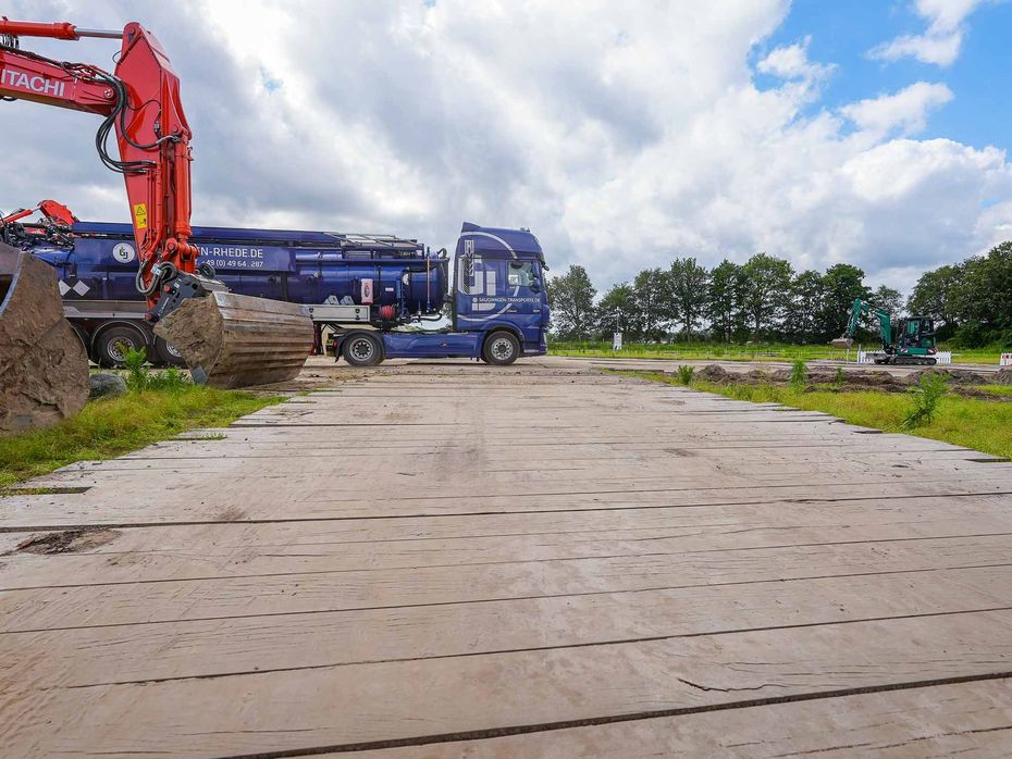 Auf einem Feldweg parkt ein blauer Saugtankwagen neben einem roten Bagger.