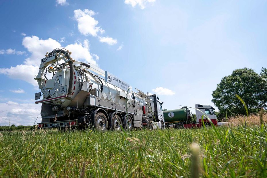 Auf einer Wiese parkt ein Saugwagen neben einem Sattelschlepper.