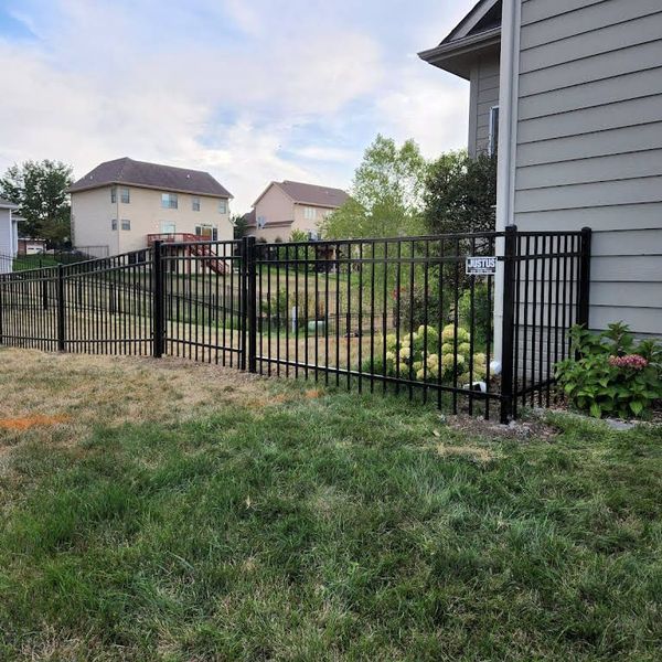 Black metal fence in a yard next to a house.