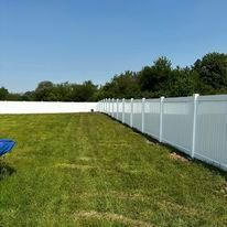 White vinyl fence surrounds a green grassy yard under a blue sky.