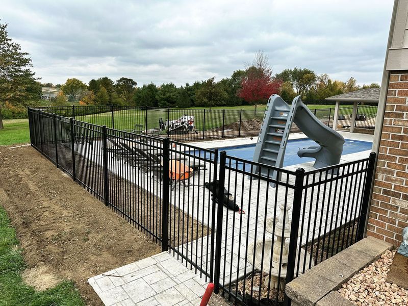 Black metal fence surrounds a swimming pool with a slide.