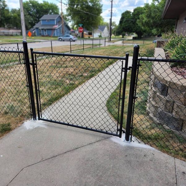 Black chain-link fence with gate on a concrete walkway leading to a sidewalk.