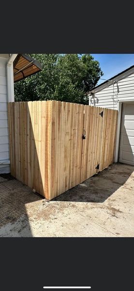 Wooden fence encloses a corner, beside a white house and a garage. 