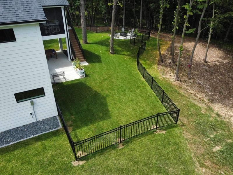 Black fence bordering a green lawn next to a white house with a deck and stairs.