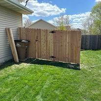 Wooden fence with a gate in a grassy backyard, trash can beside it.