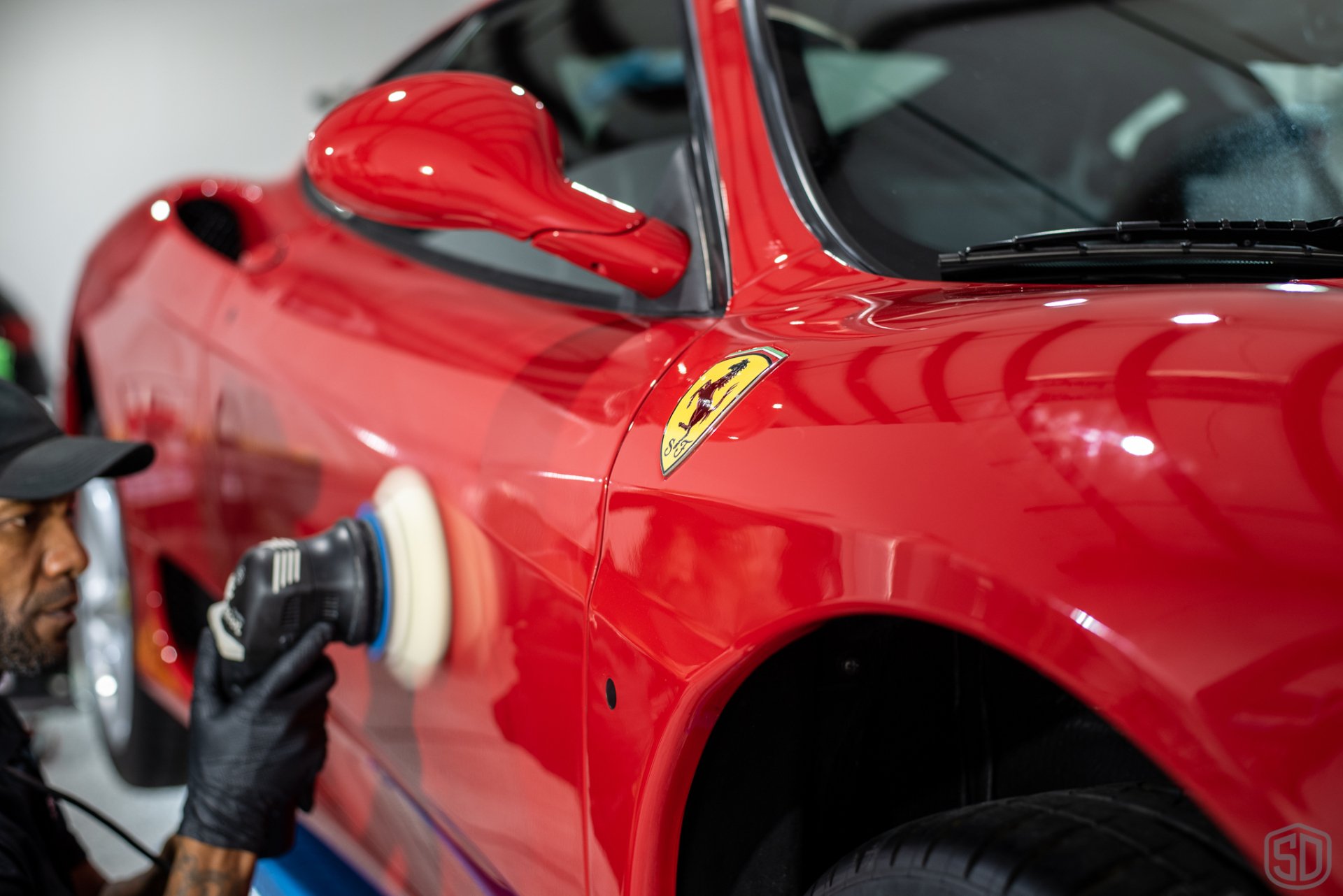 A man is polishing a red car with a machine.