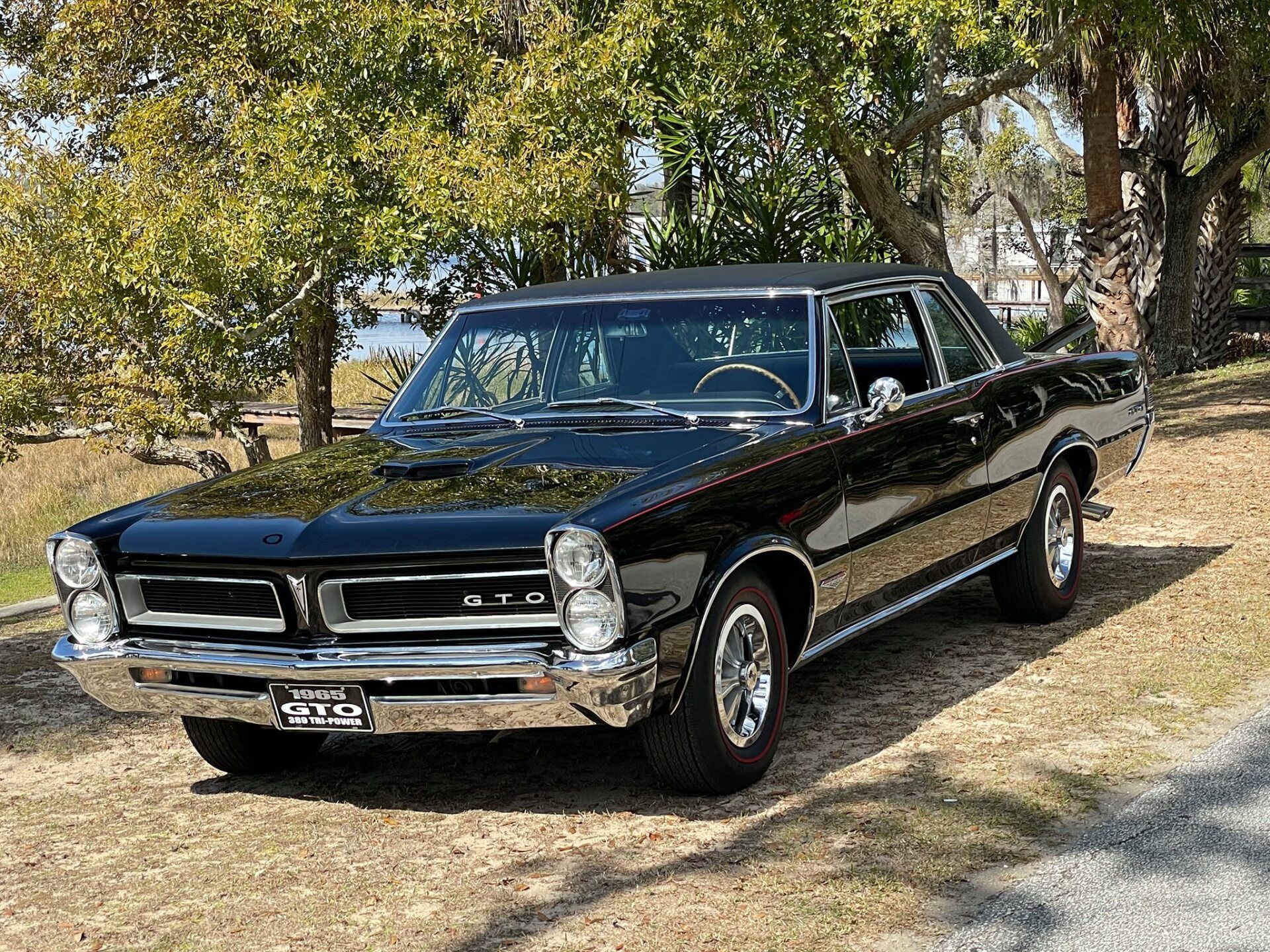 A black car is parked on the side of the road next to trees.