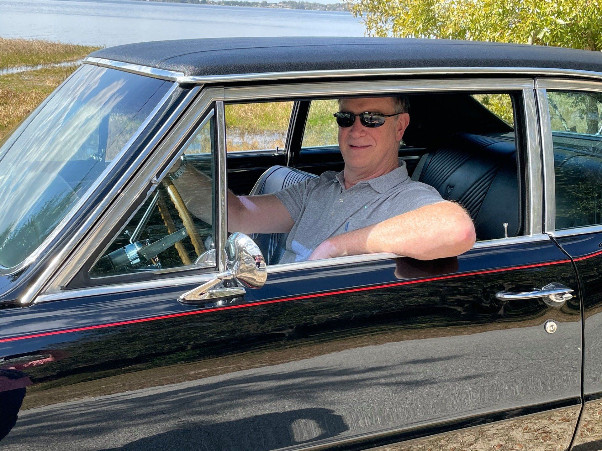 A man wearing sunglasses is sitting in a black car.