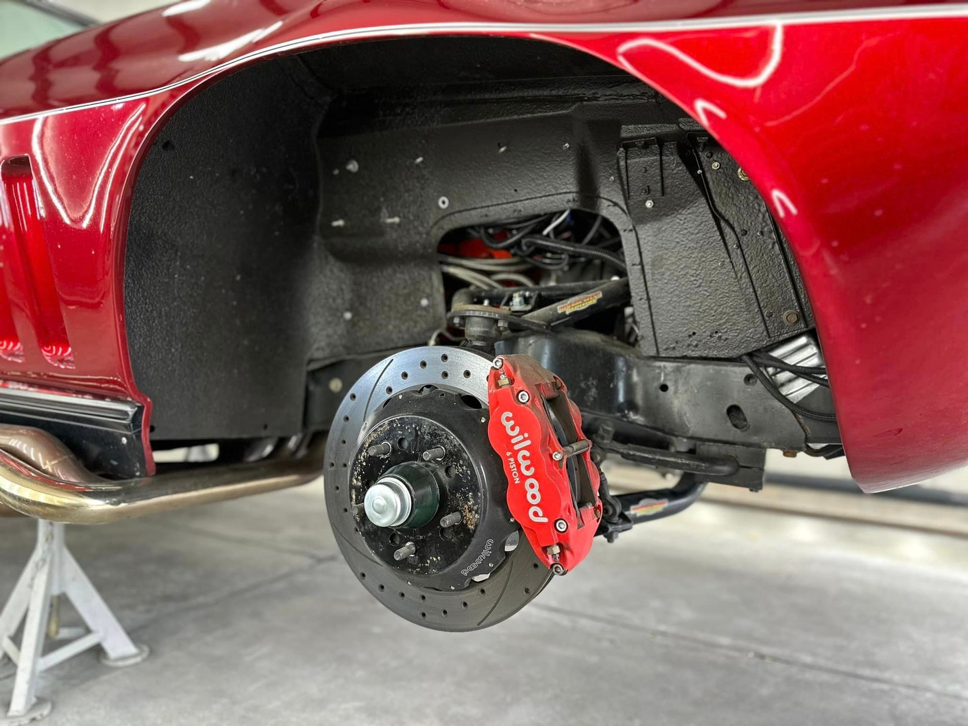 A red car with a red brake caliper is parked in a garage.