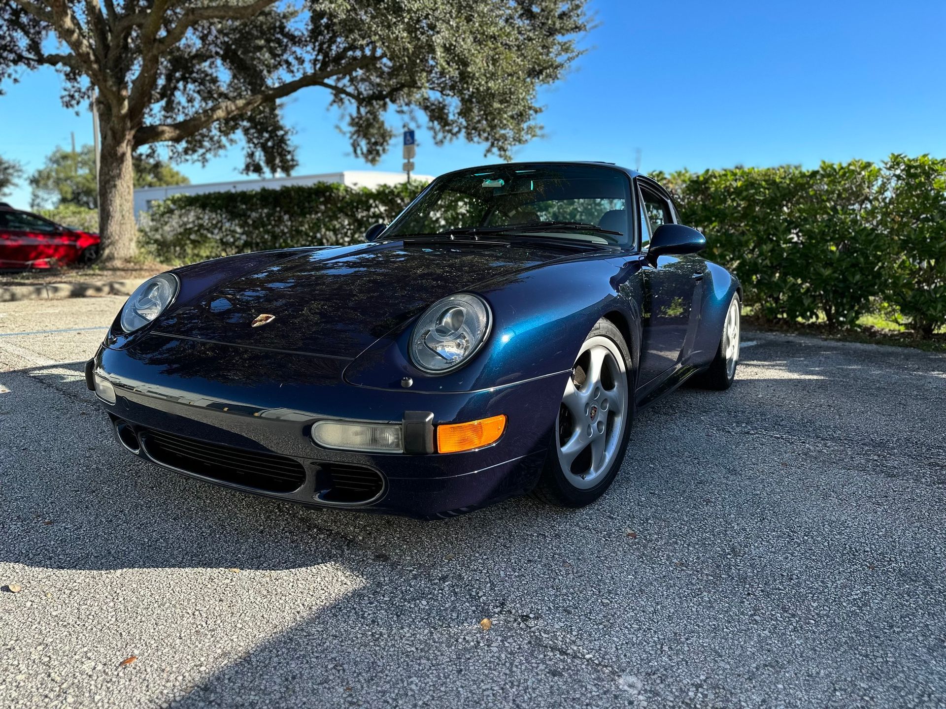 A blue porsche 911 is parked in a gravel lot.