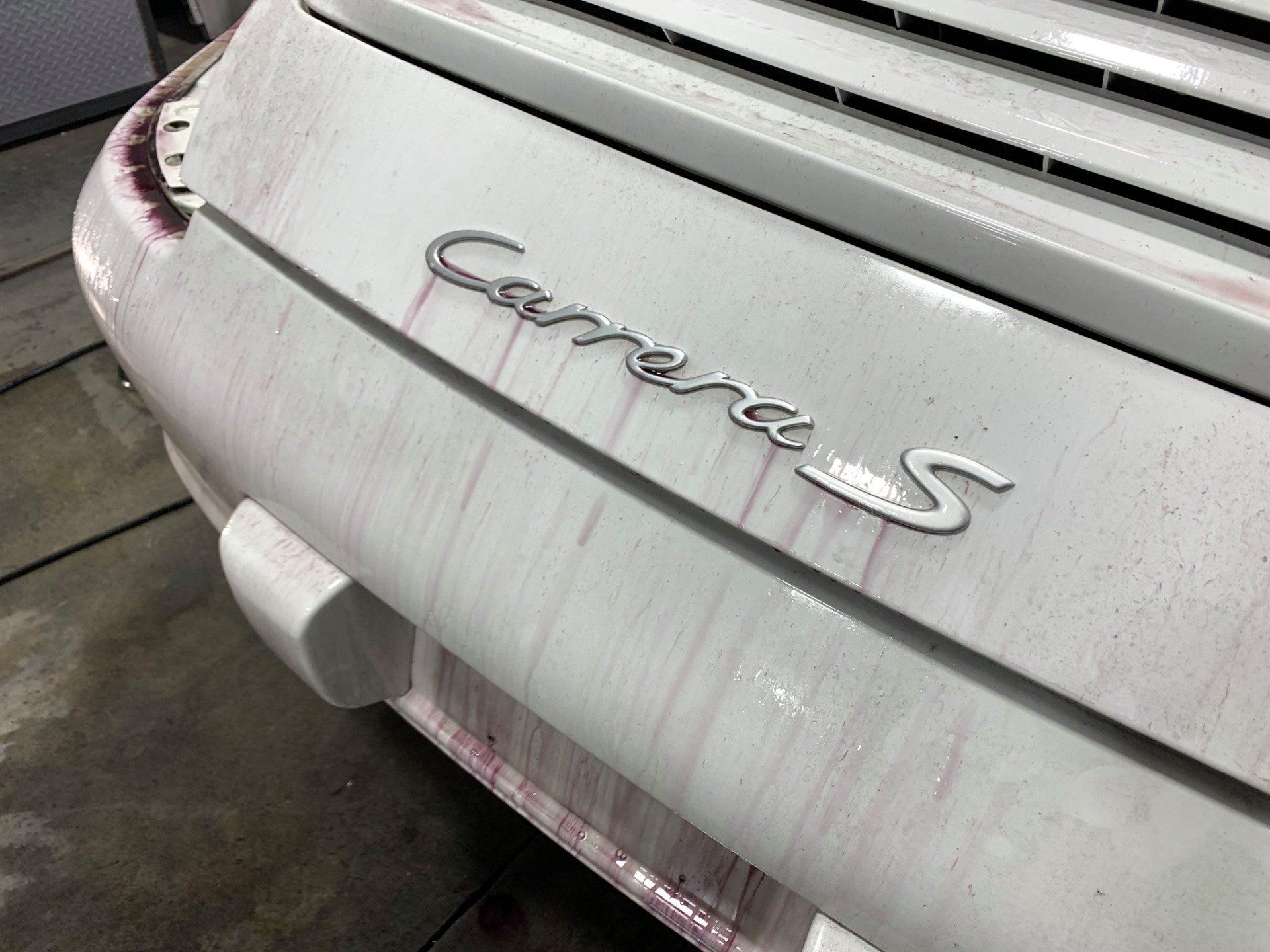 The hood of a white porsche carrera s is covered in red stains.