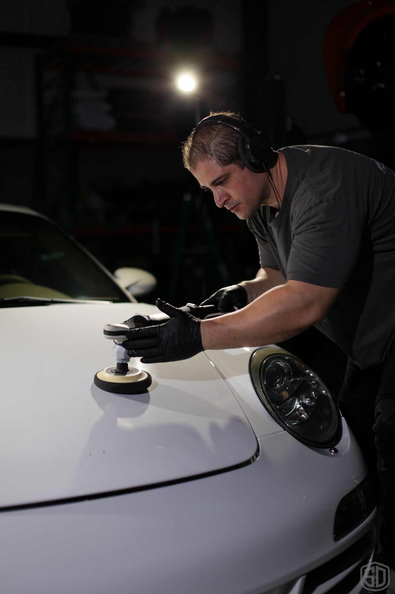 A man is polishing the hood of a white car.