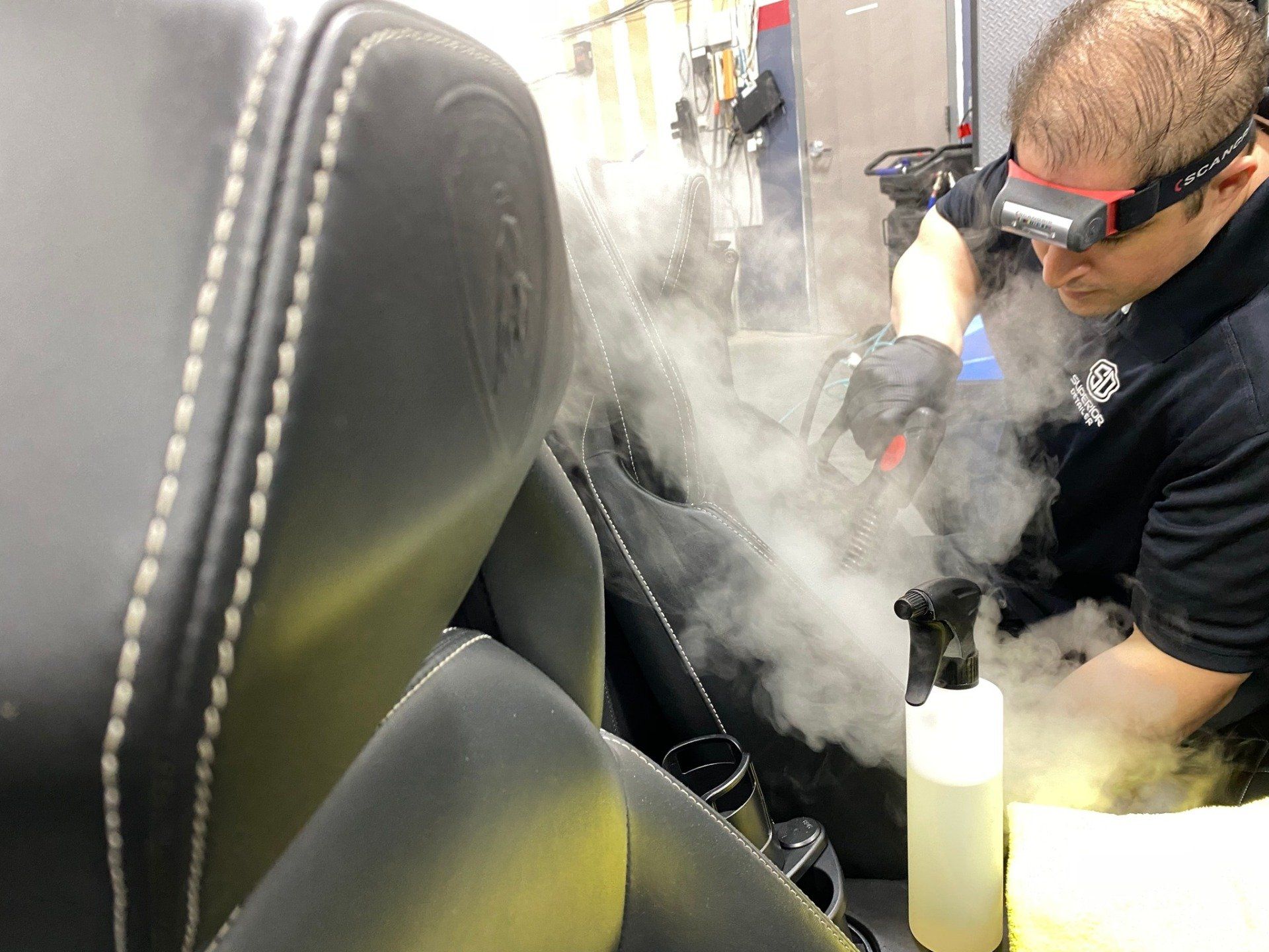 A man wearing goggles is cleaning a car seat with steam.