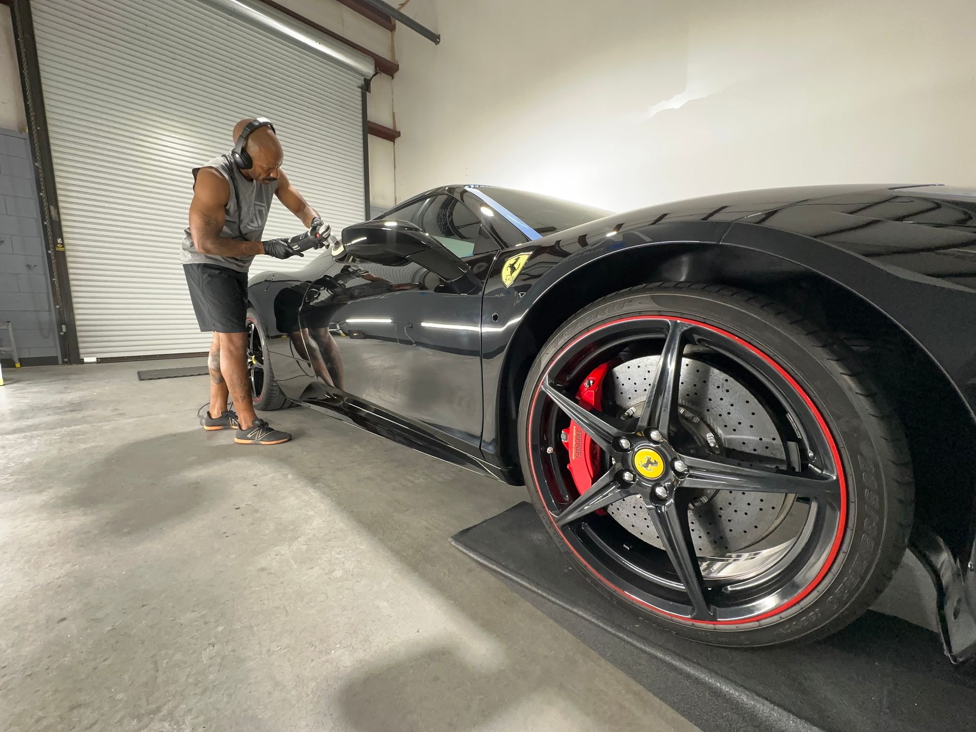 A man is standing next to a black sports car in a garage.