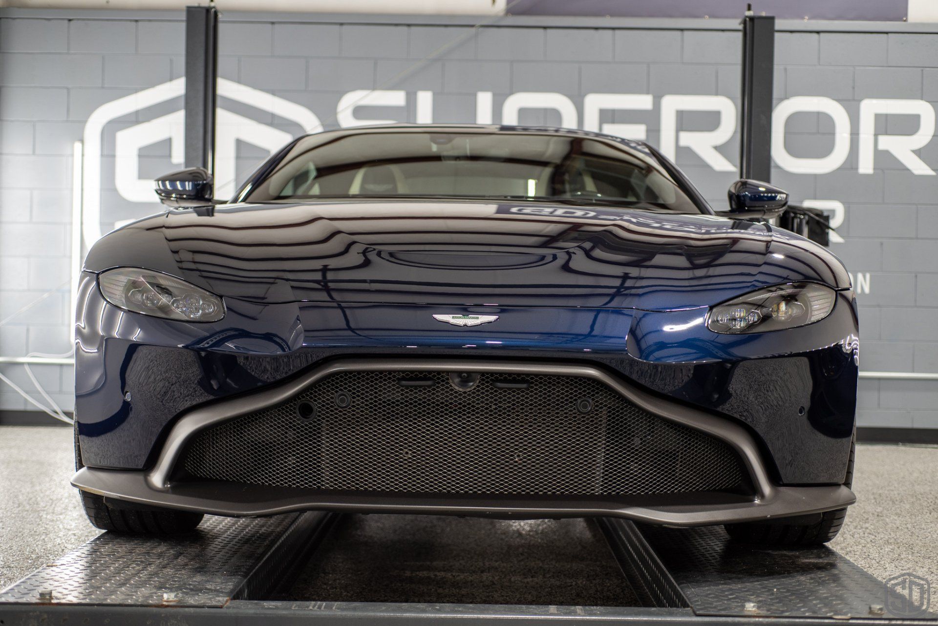 A blue aston martin vantage is parked on a lift in a garage.