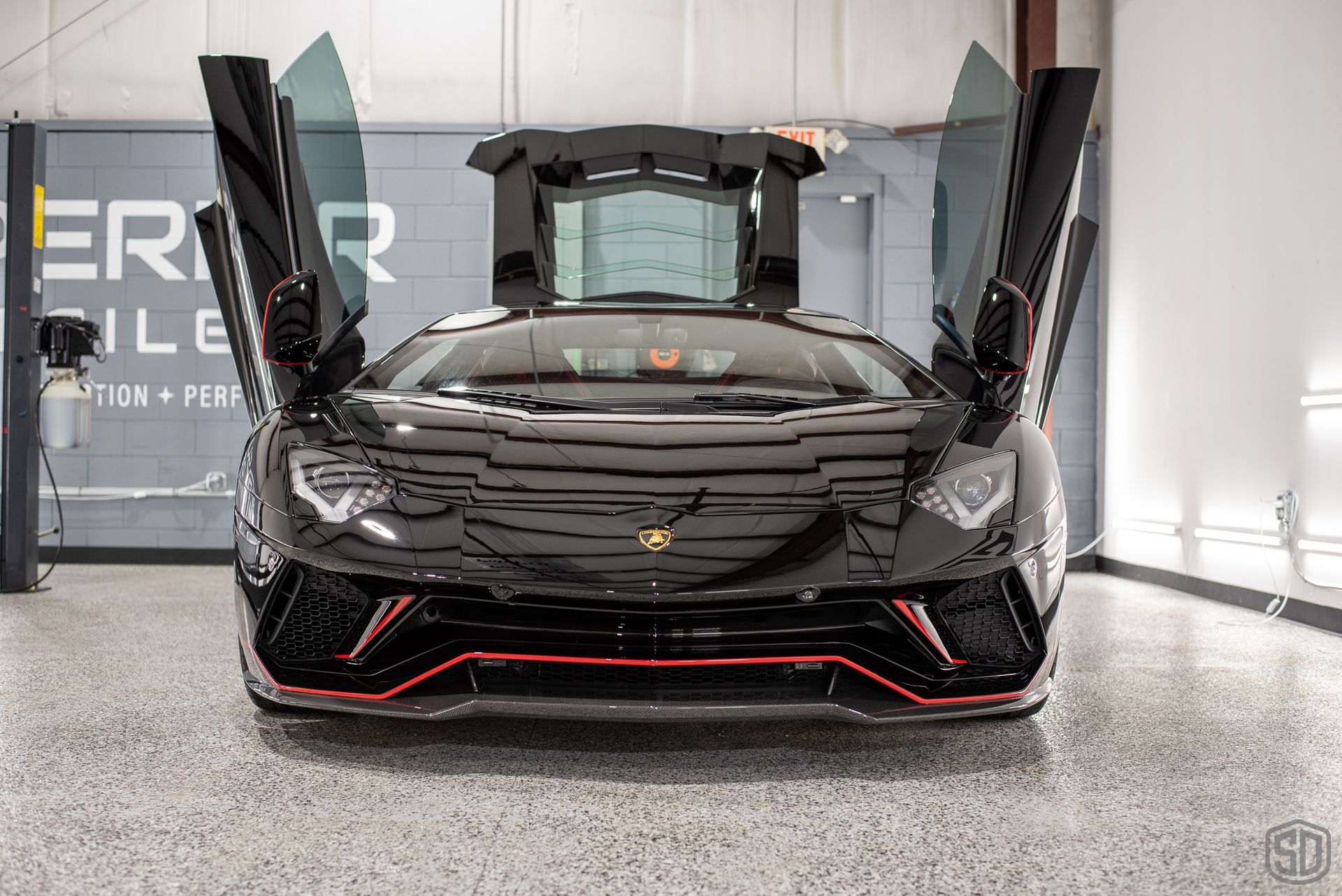 A black lamborghini aventador is parked in a garage with its doors open.