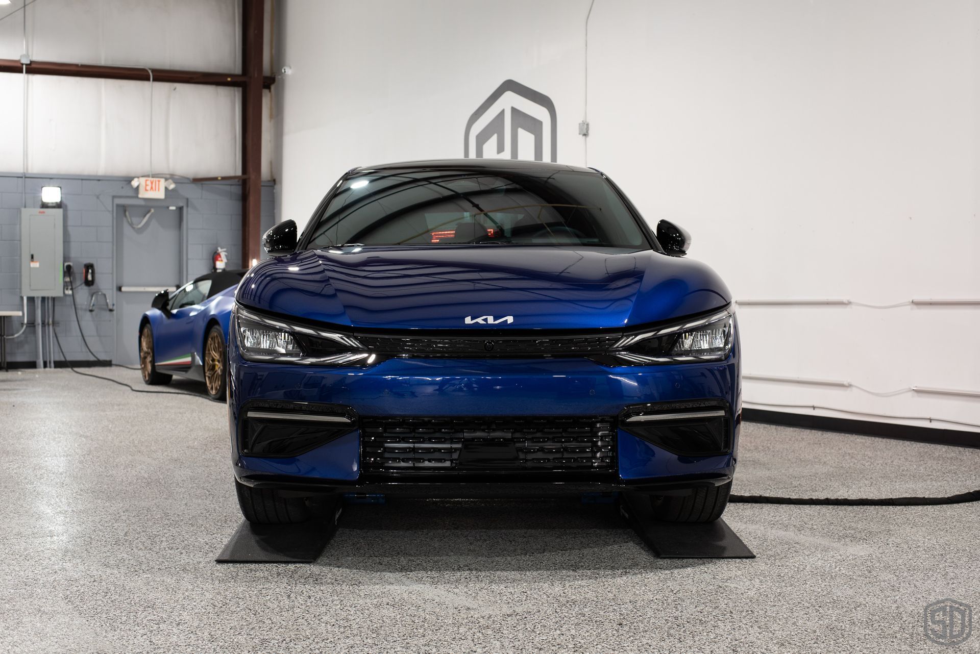 A blue car is parked in a garage next to another car.