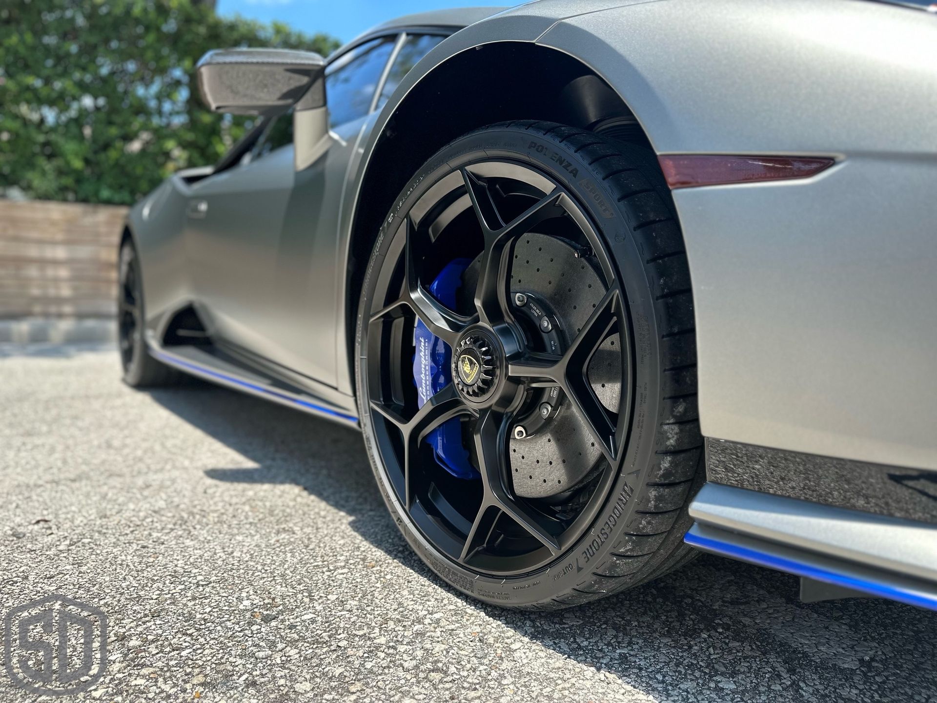 A silver sports car with black wheels and blue brake calipers is parked on the side of the road.